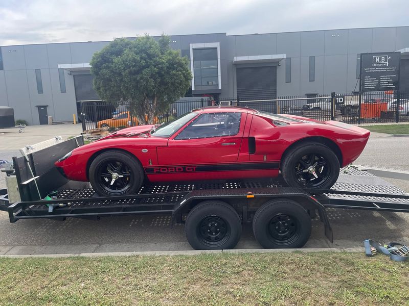 Red RF GT40 in side profile, loaded on a car trailer outside the workshop
