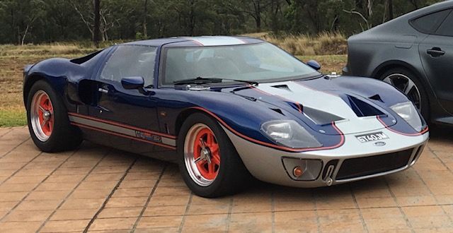 Navy blue GT40-style car with orange wheels, front three quarter view on brick paving