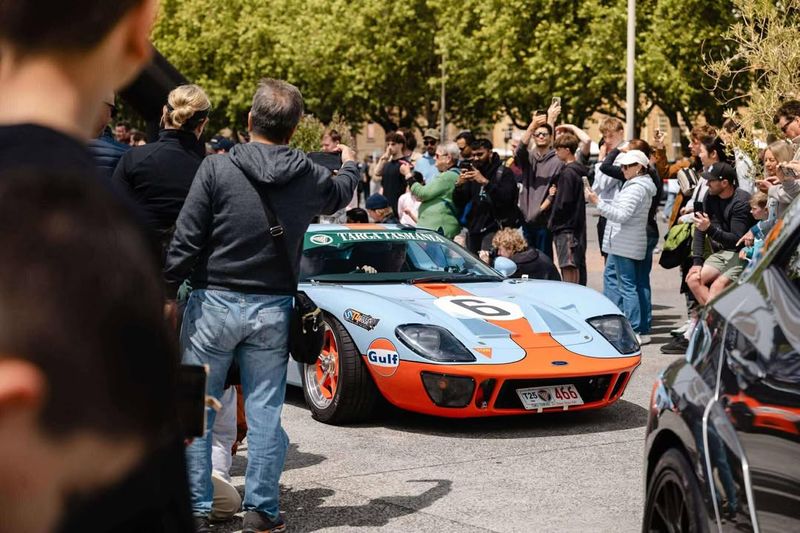 Heritage blue and marigold liveried GT40 with race number 6 and a Targa Tasmania banner, surrounded by a crowd photographing it in a city plaza