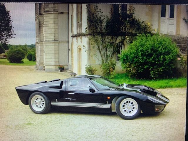 Black GT40, side profile, parked on a gravel driveway in front of a stone building