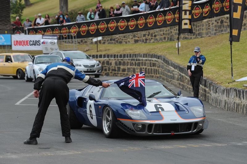 Navy blue GT40 with a white centre stripe and number 6, a race marshal holding an Australian flag beside it